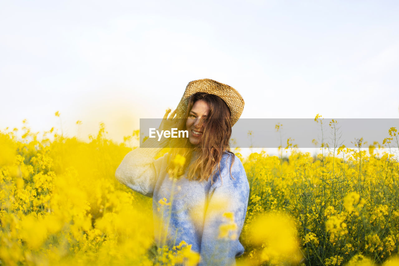 Young woman with yellow flowers on field against sky