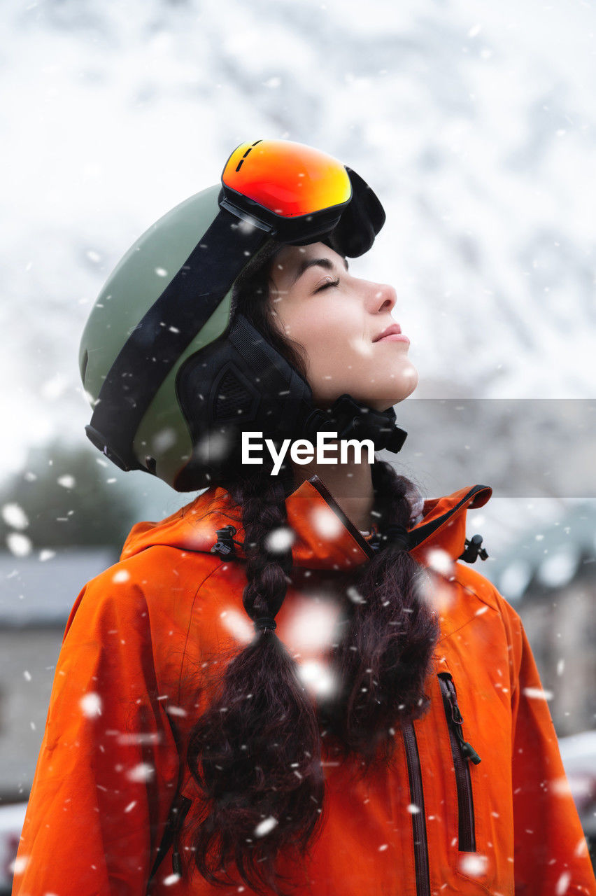 Smiling young woman, portrait, standing and enjoying snowfall, wearing protective clothing, helmet