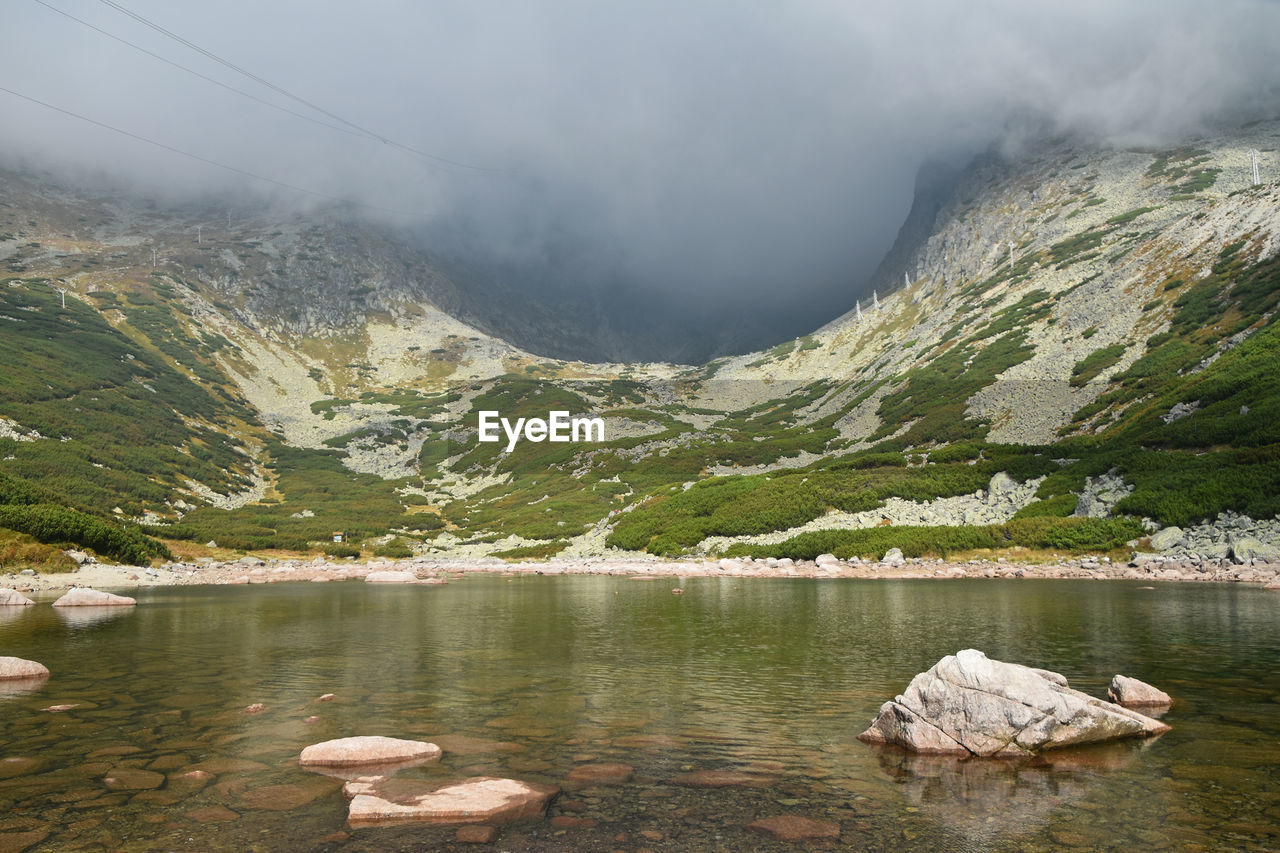 Scenic view of lake by mountains against cloudy sky