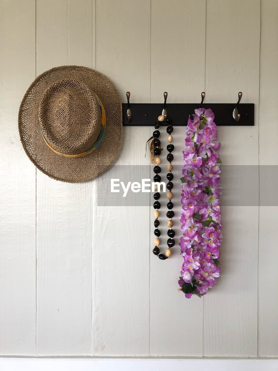 Close-up of straw hat with bead necklace and garland hanging on hooks at home