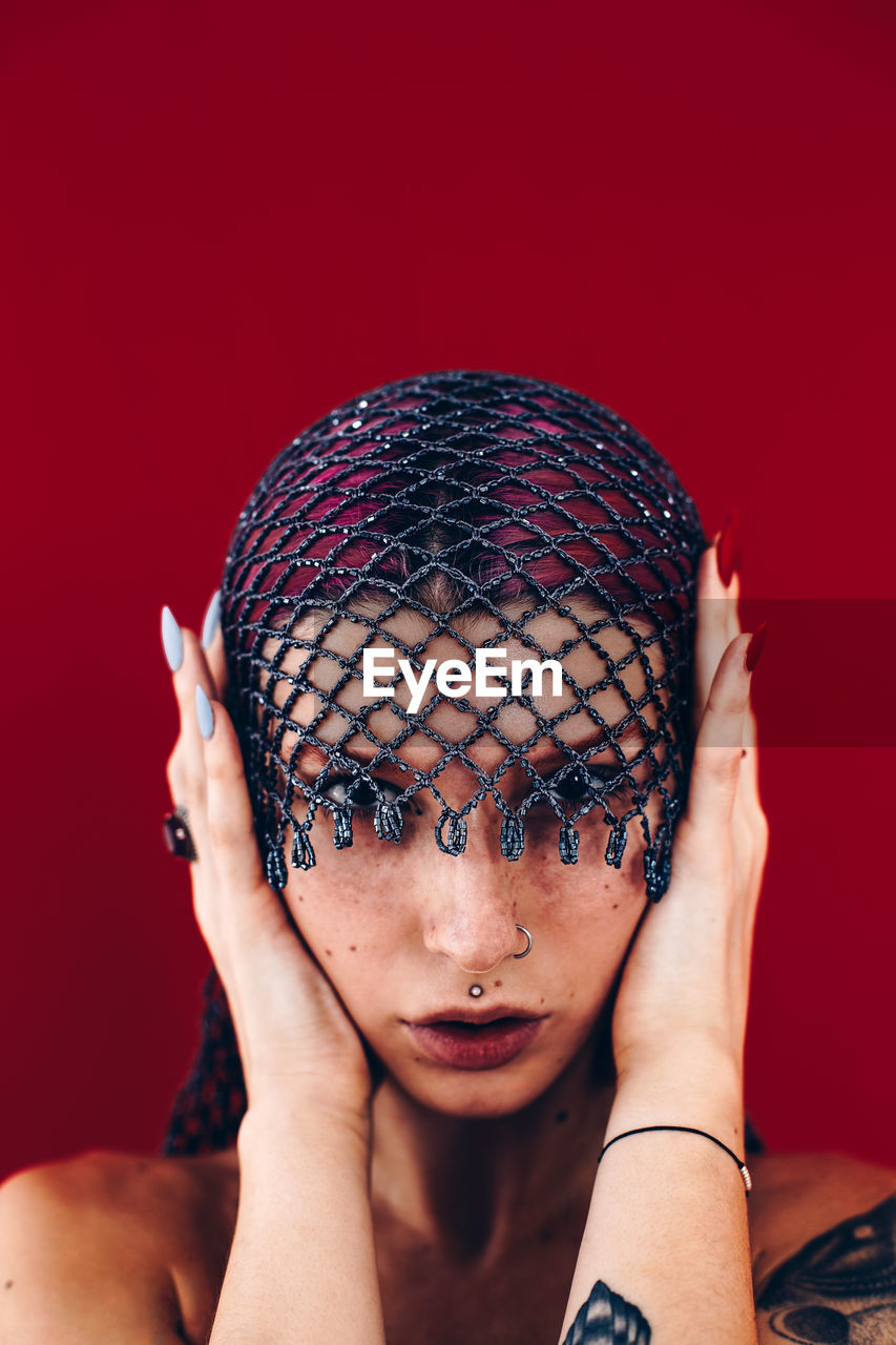 Close-up portrait of beautiful woman wearing net scarf against red background