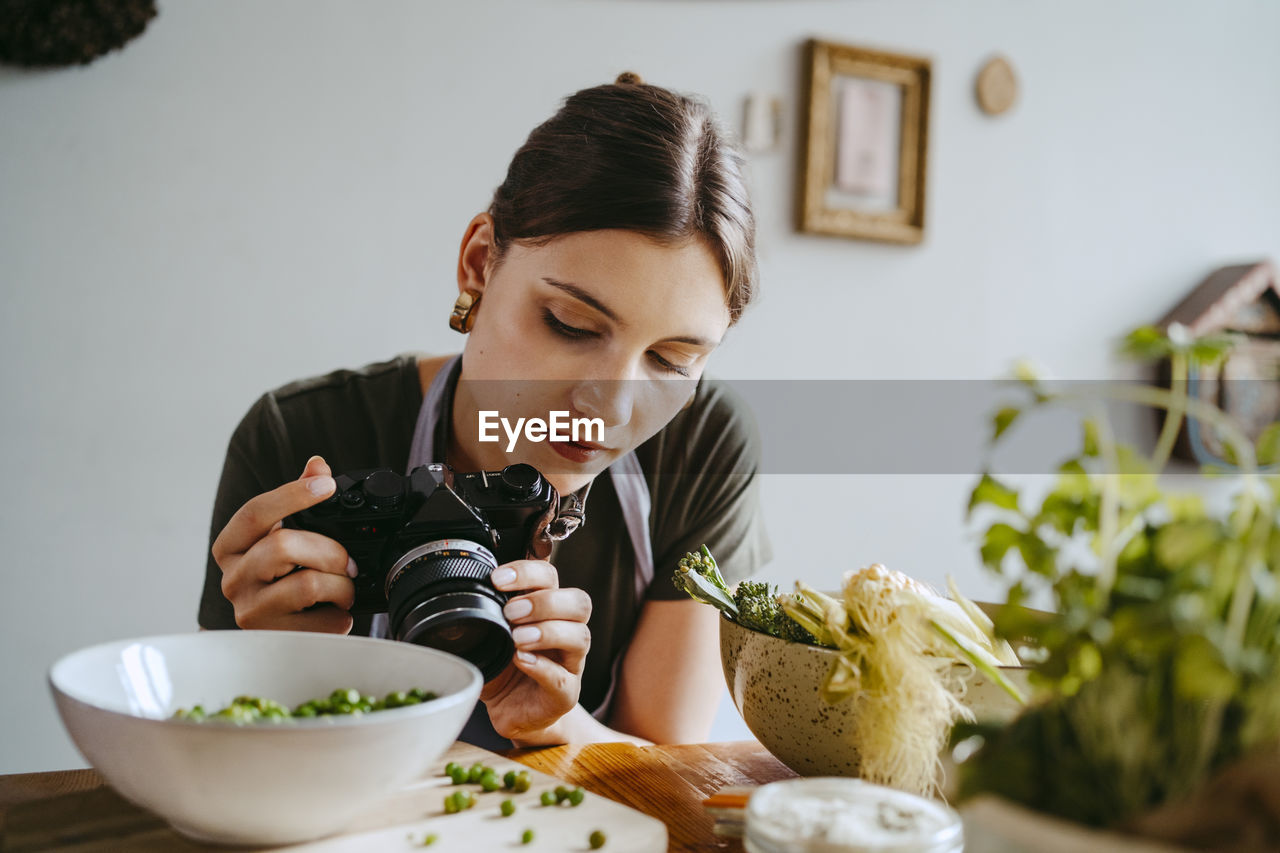 Food stylist adjusting camera lens while photographing green peas in studio