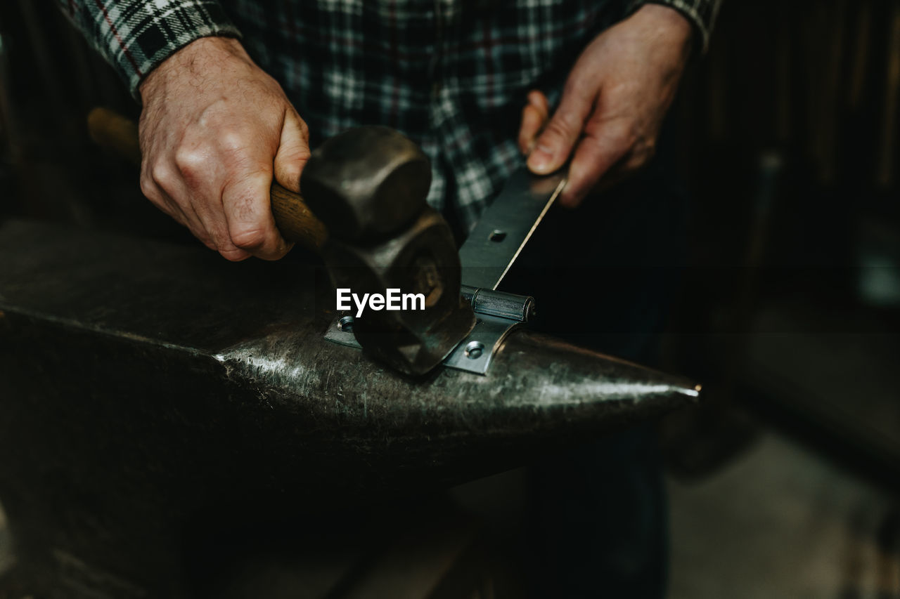 Midsection of man hammering latch in workshop