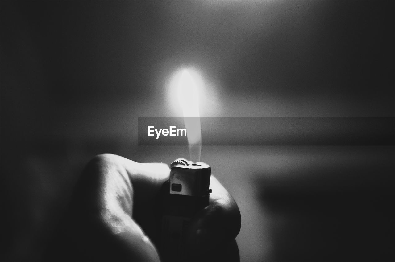 Close-up of hand holding cigarette lighter with flame at night