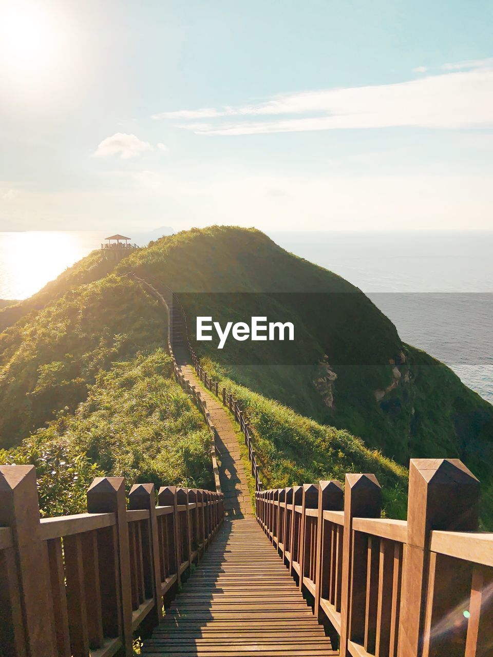 Footbridge leading towards mountains by sea against sky