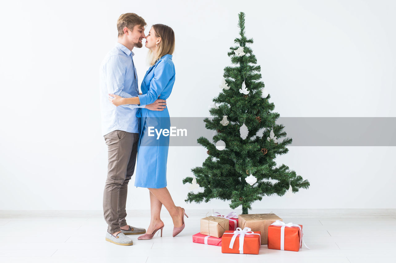 Full length of young woman standing in front of christmas tree