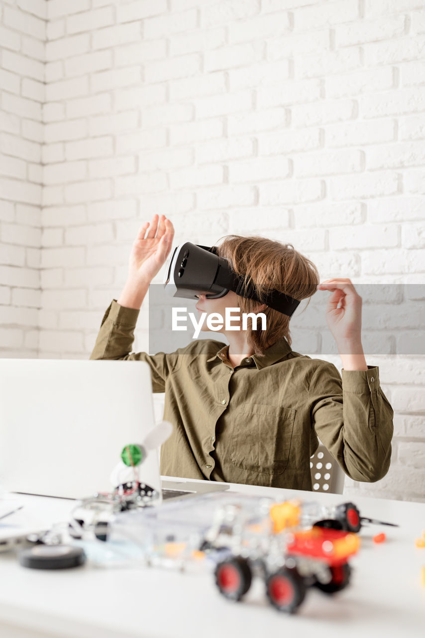 Nice teen boy in vr glasses sitting at the table playing game