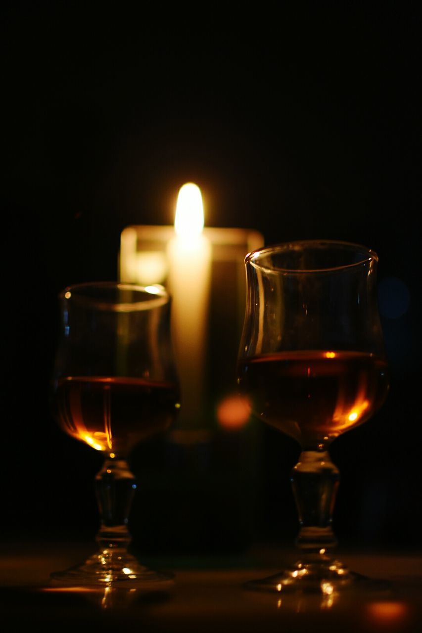 Close-up of wineglasses by burning candle on table in darkroom