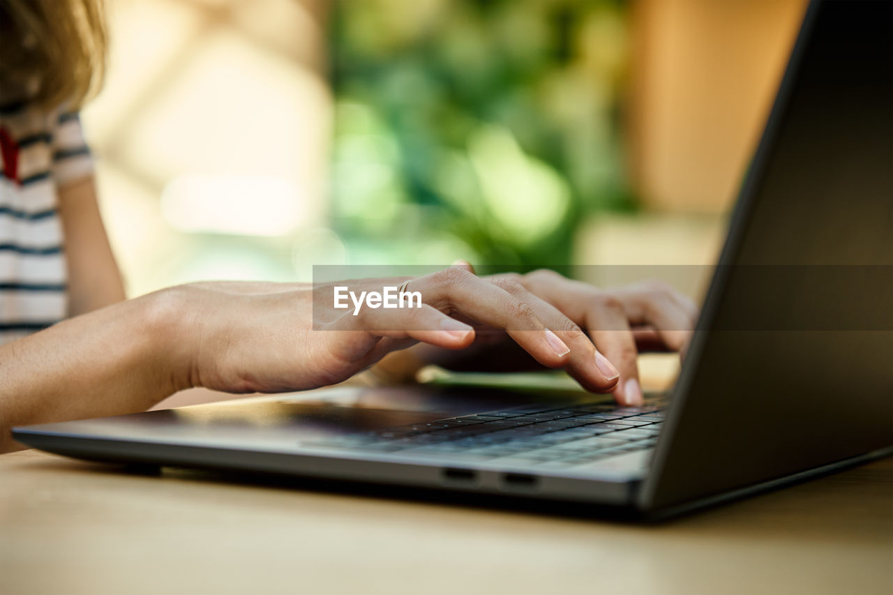 Hands typing on laptop keyboard. close up shot of woman using laptop in cafe