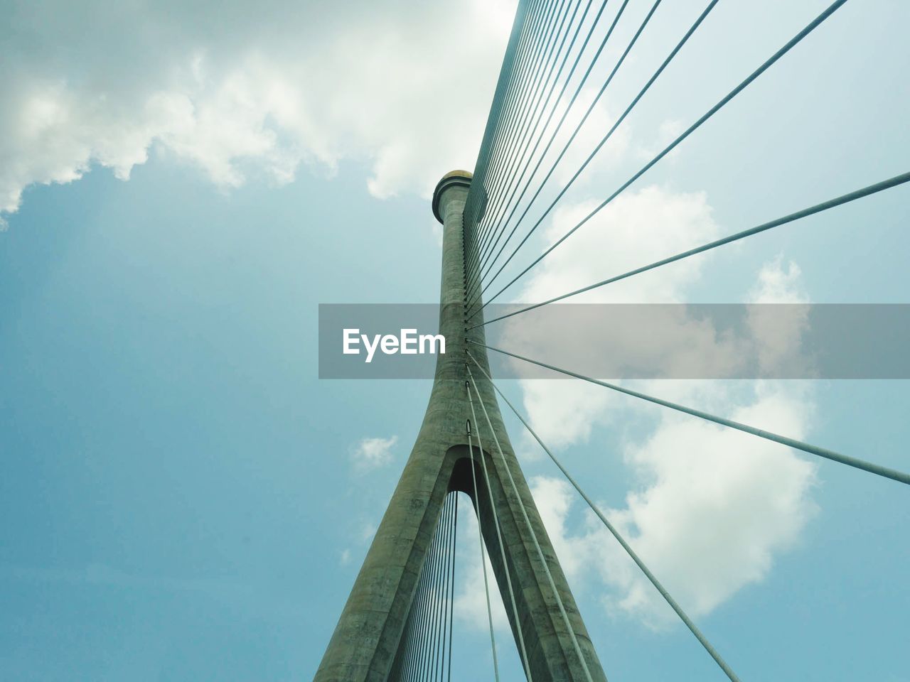 Low angle view of suspension bridge against cloudy sky