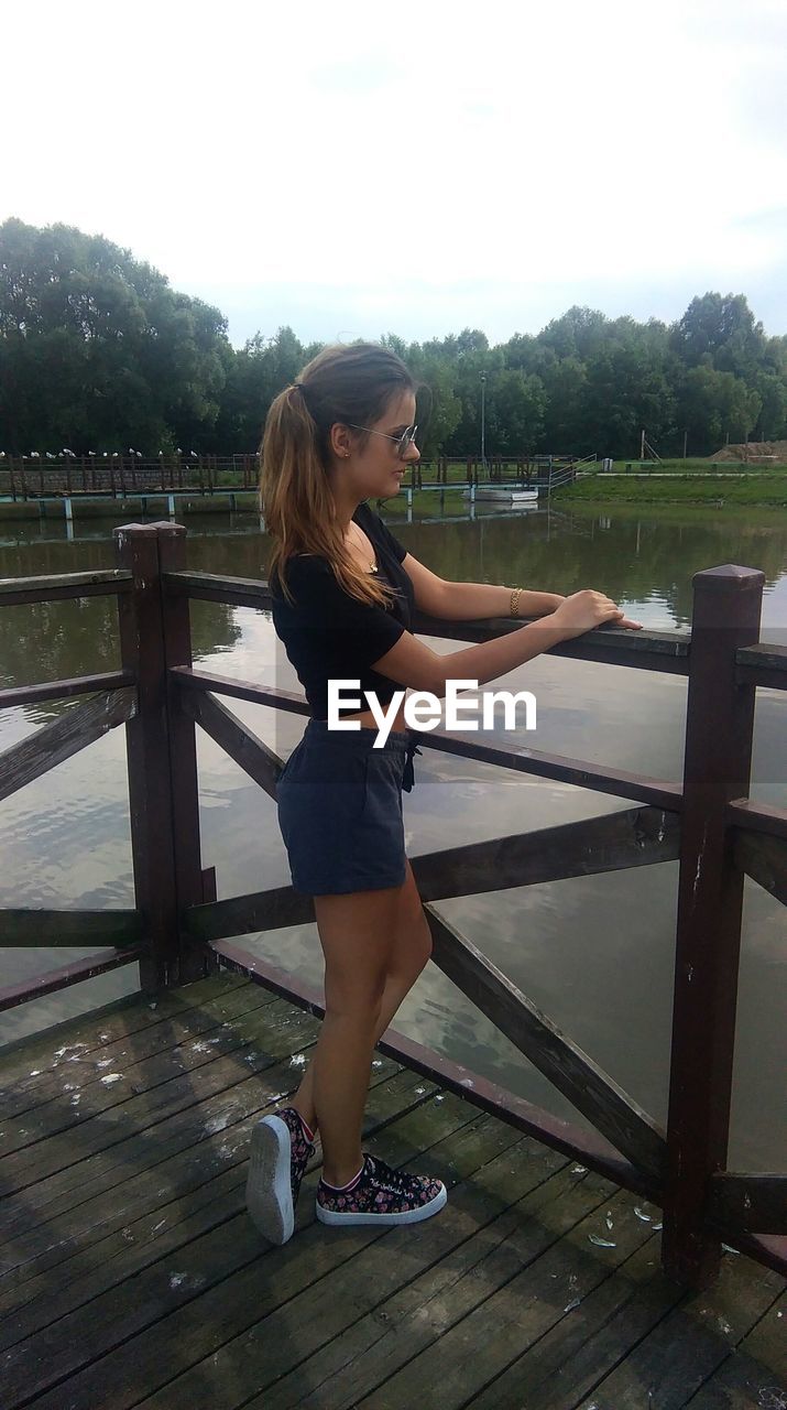 Side view of young woman standing on pier over lake