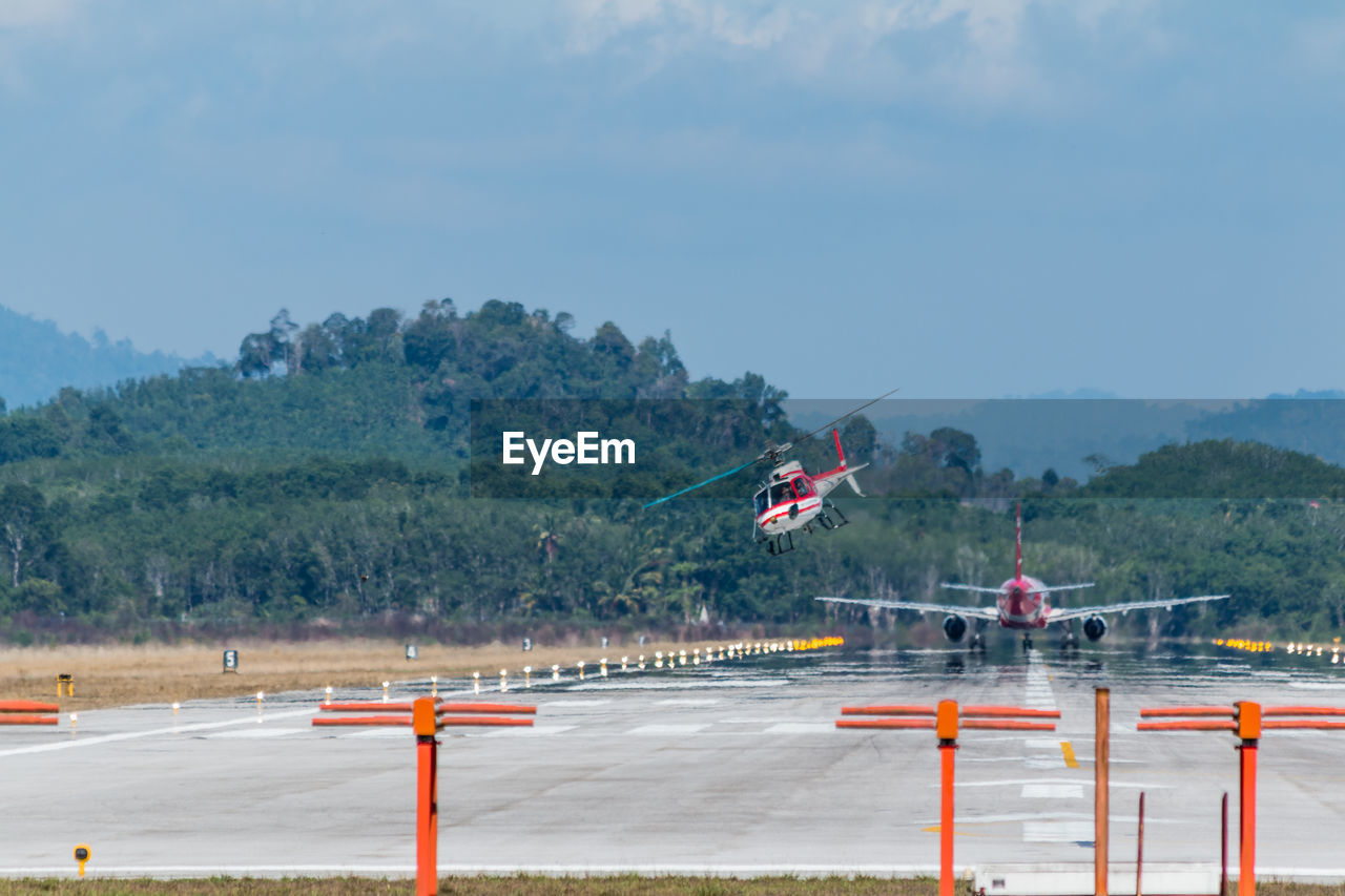 Airplane and helicopter at airport runway against sky on sunny day