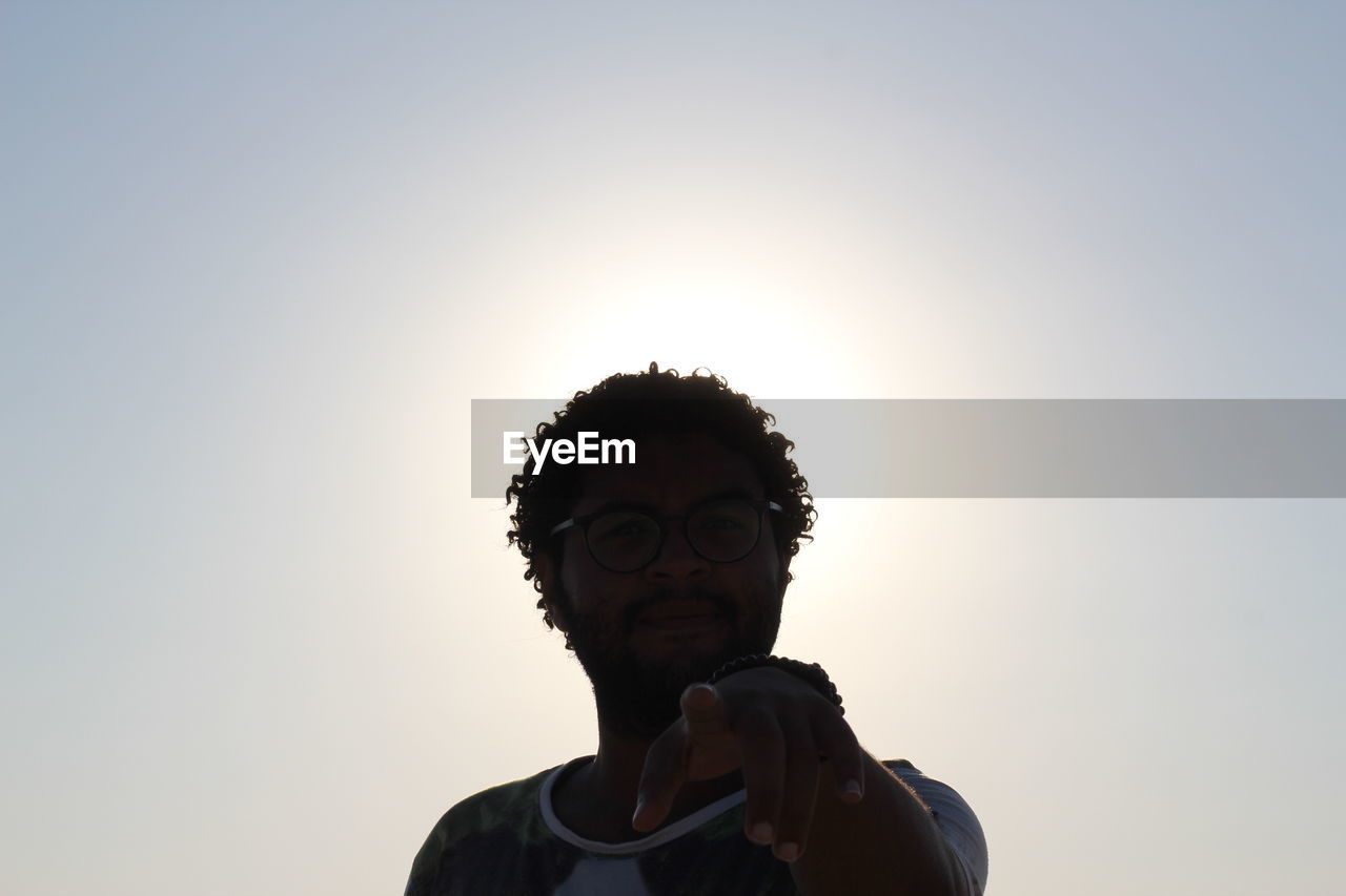 Low angle view of young man pointing against clear sky during sunset
