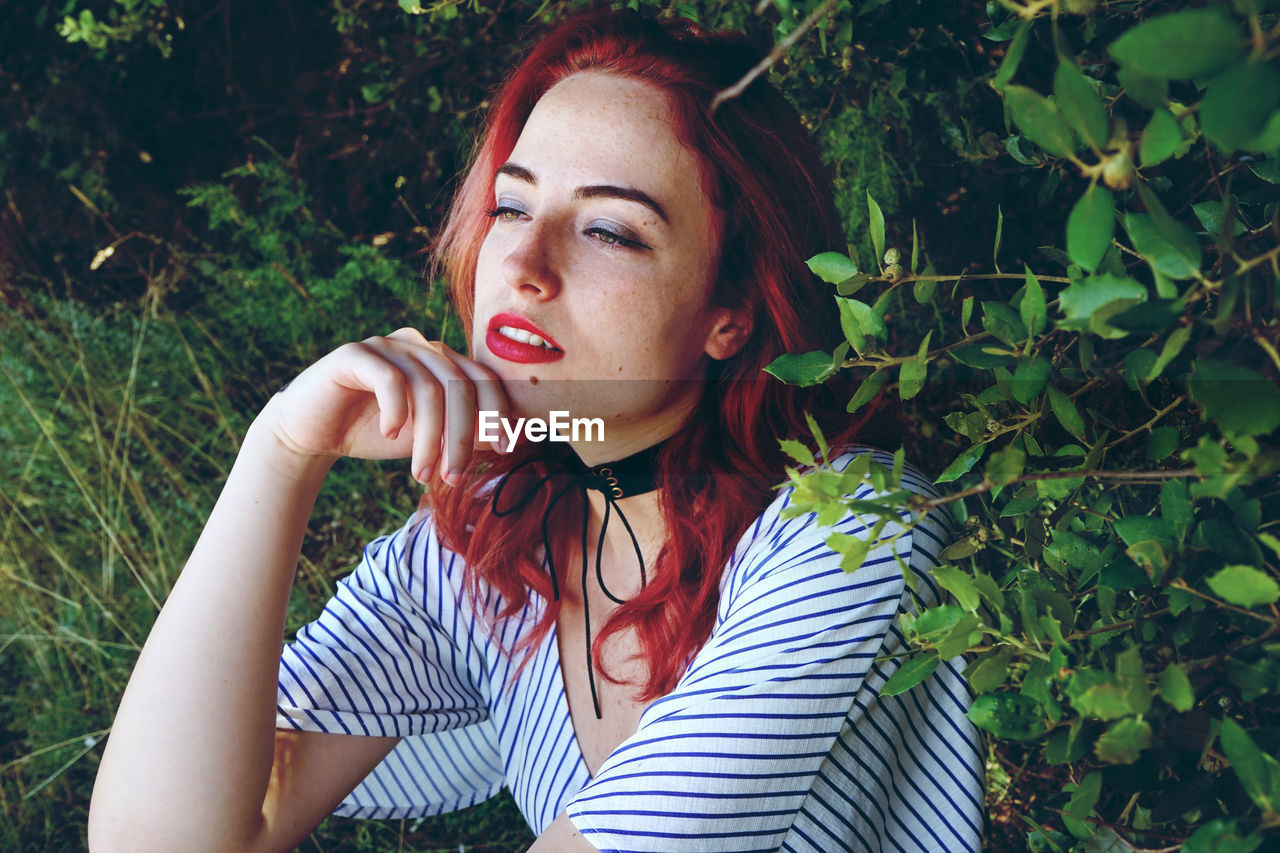 Beautiful young woman with redhead sitting amidst plants in park