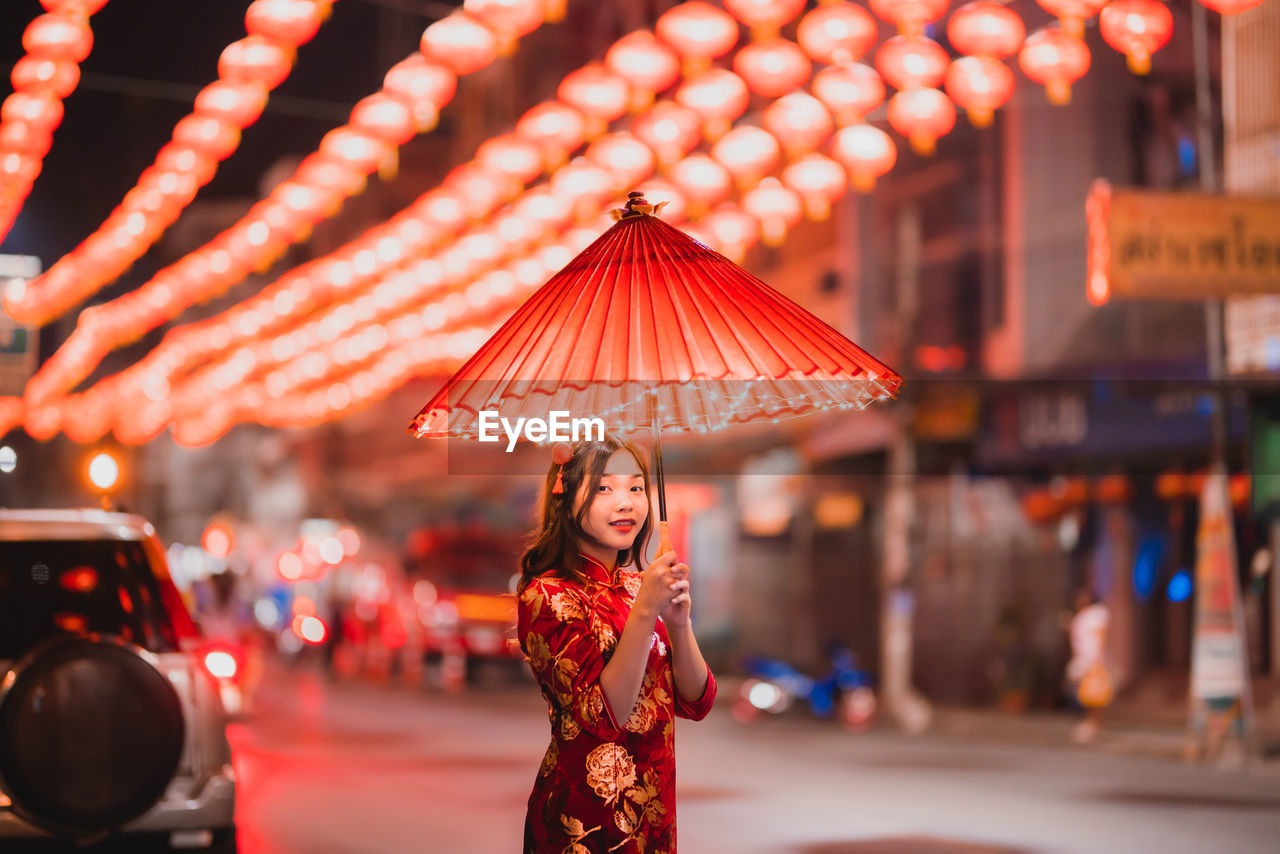 Portrait of woman with red umbrella standing on street