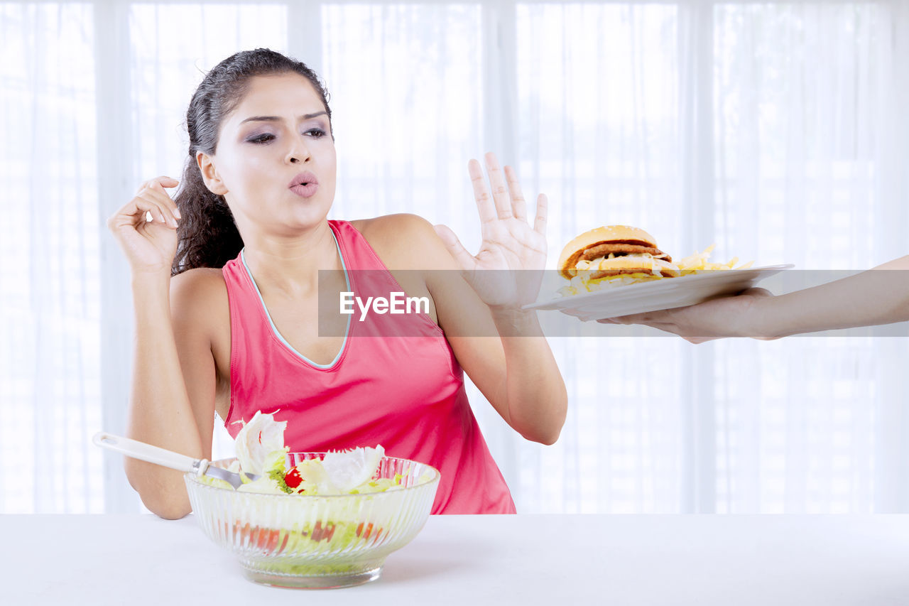 Woman with salad bowl refusing burger at home