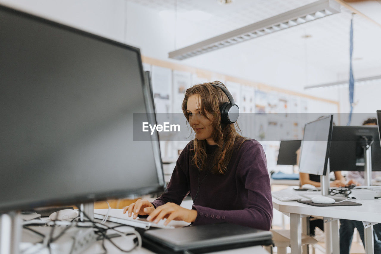 Young woman listening through headphones while using computer in school lab