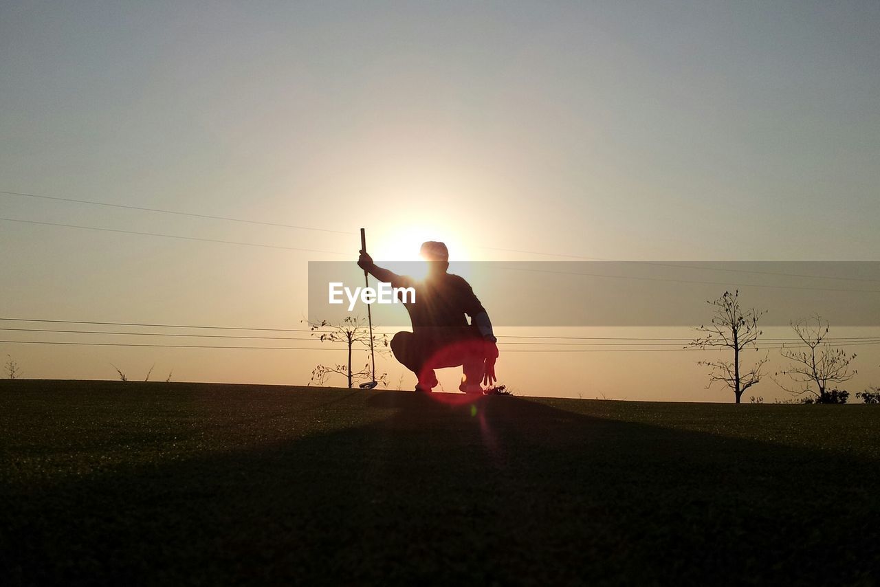 Low angle view of silhouette man crouching on golf course during sunset