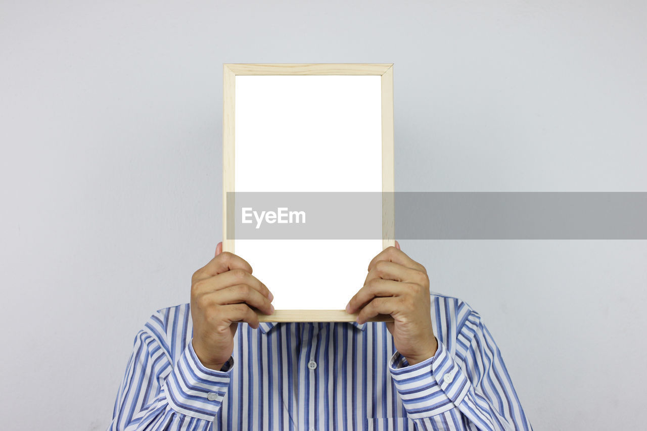 Close-up of man holding blank whiteboard against white background