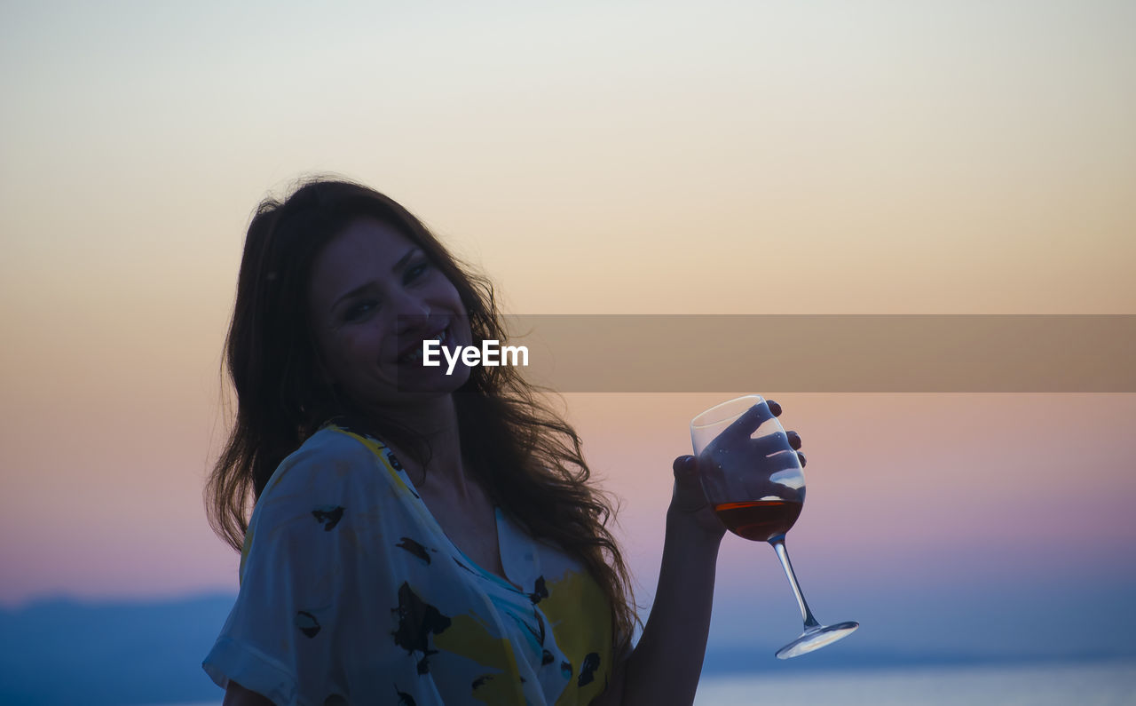 Young woman drinking red wine at sunset