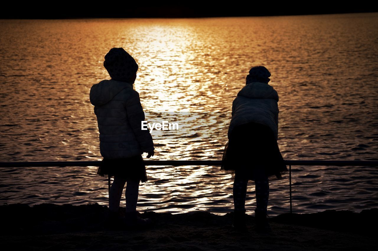 Rear view of people standing against lake during sunset