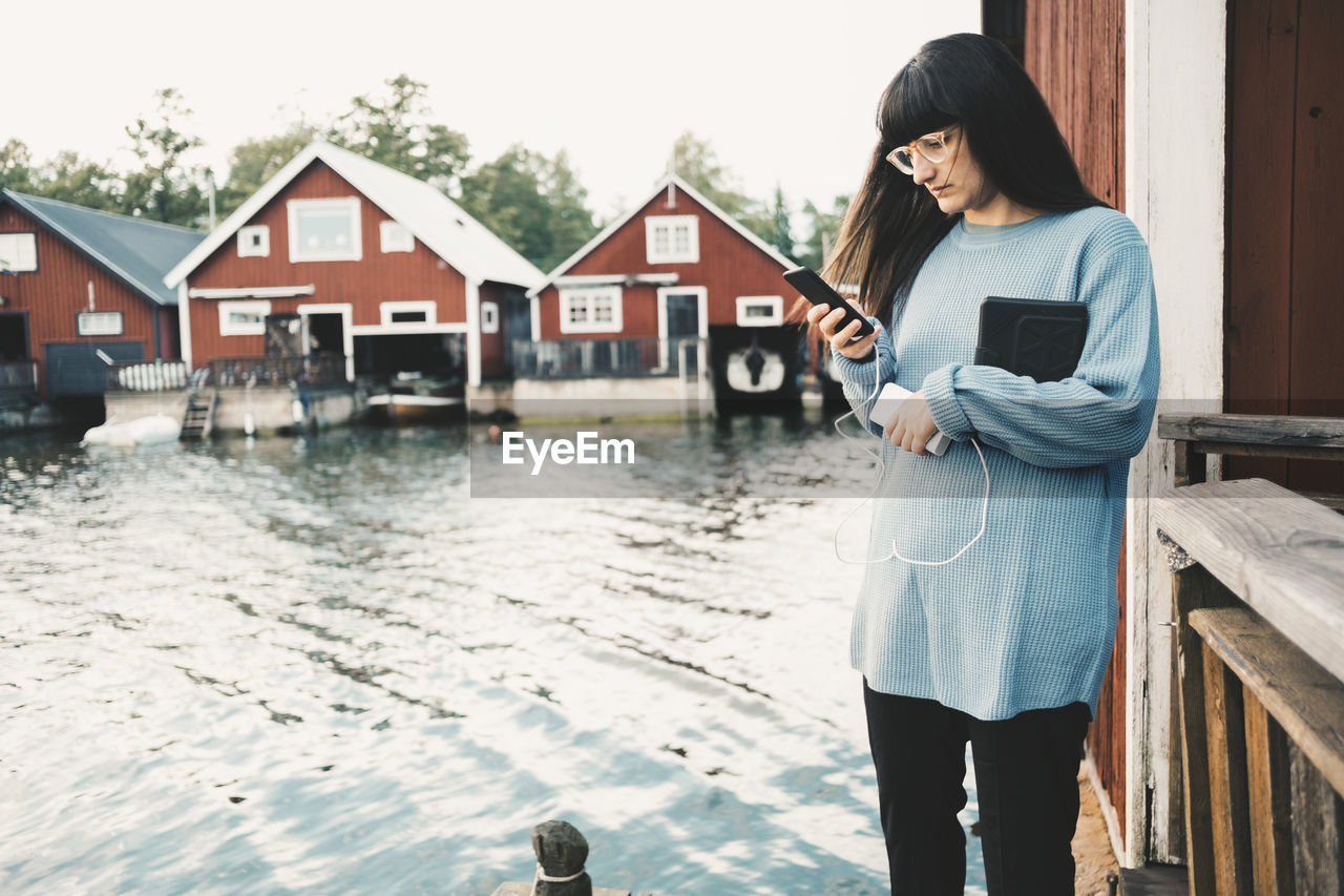 Woman using smart phone while standing by lake