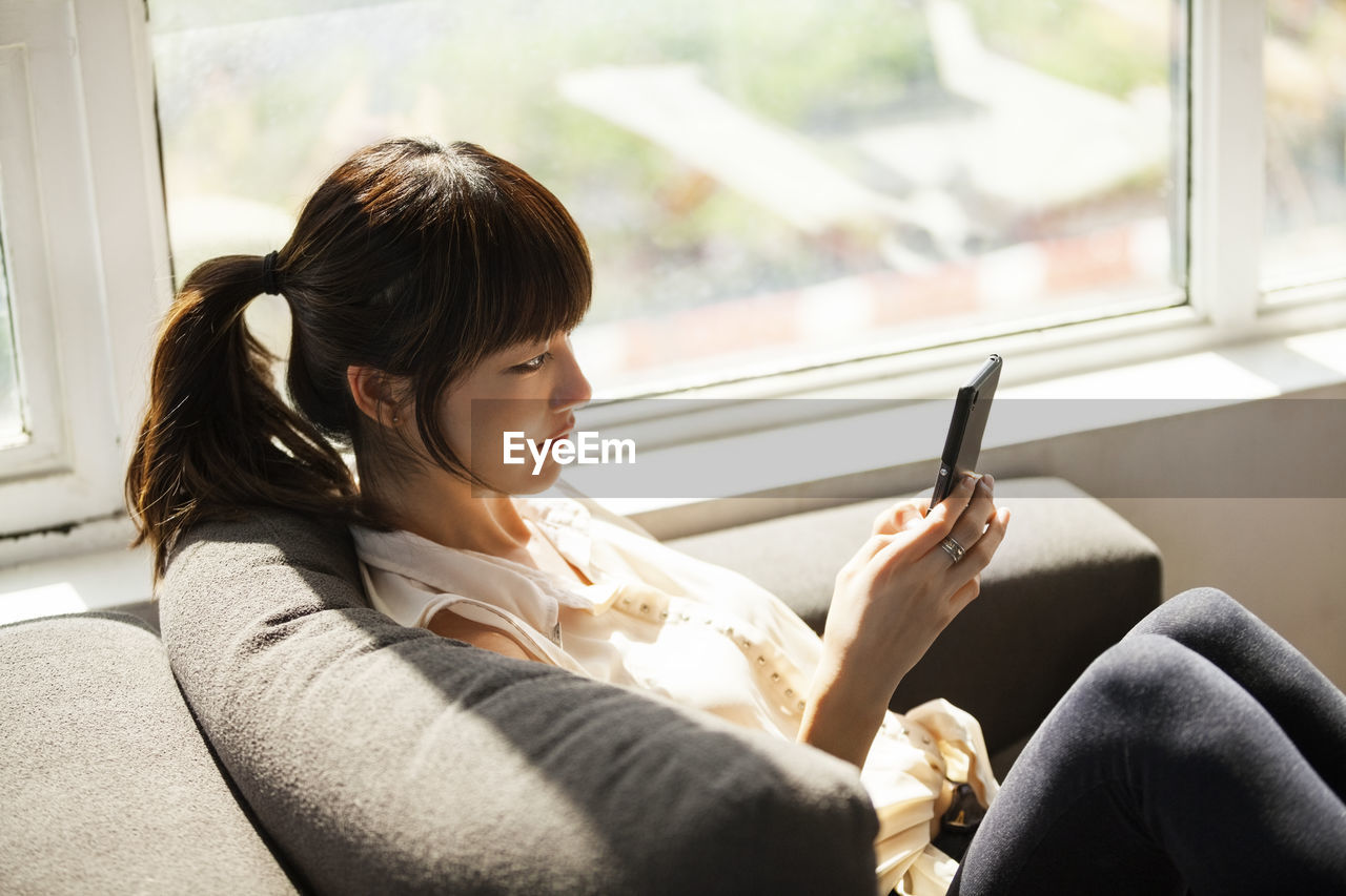 Side view of businesswoman using smart phone on sofa in creative office