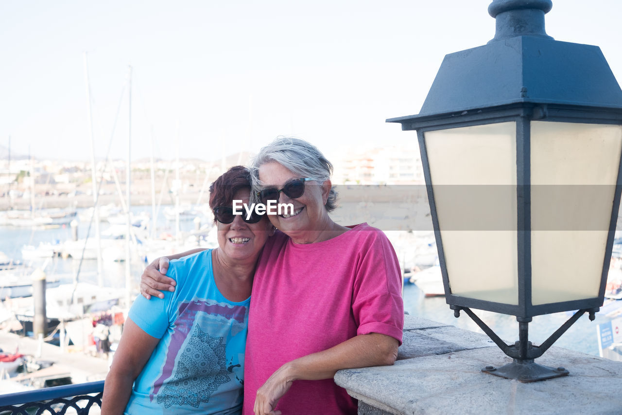 Portrait of smiling friends standing by railing at harbor