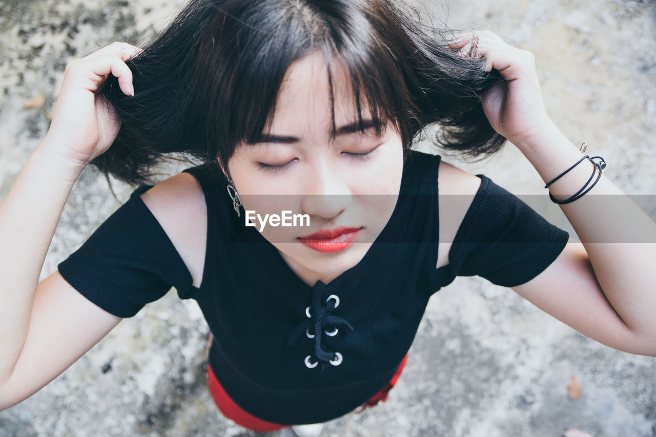 High angle of young woman with eyes closed standing on footpath