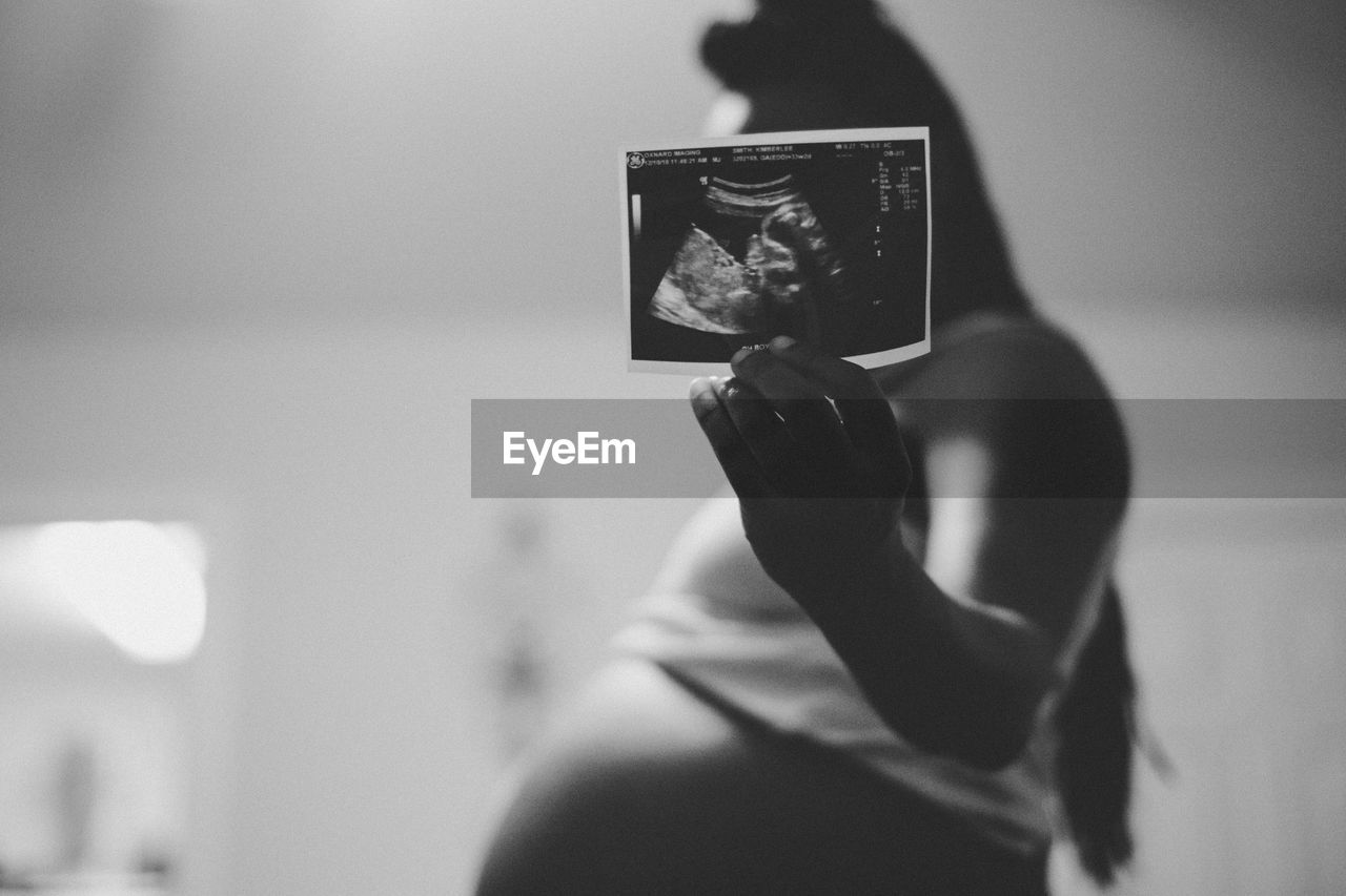 Side view of pregnant woman showing ultrasound photograph at home