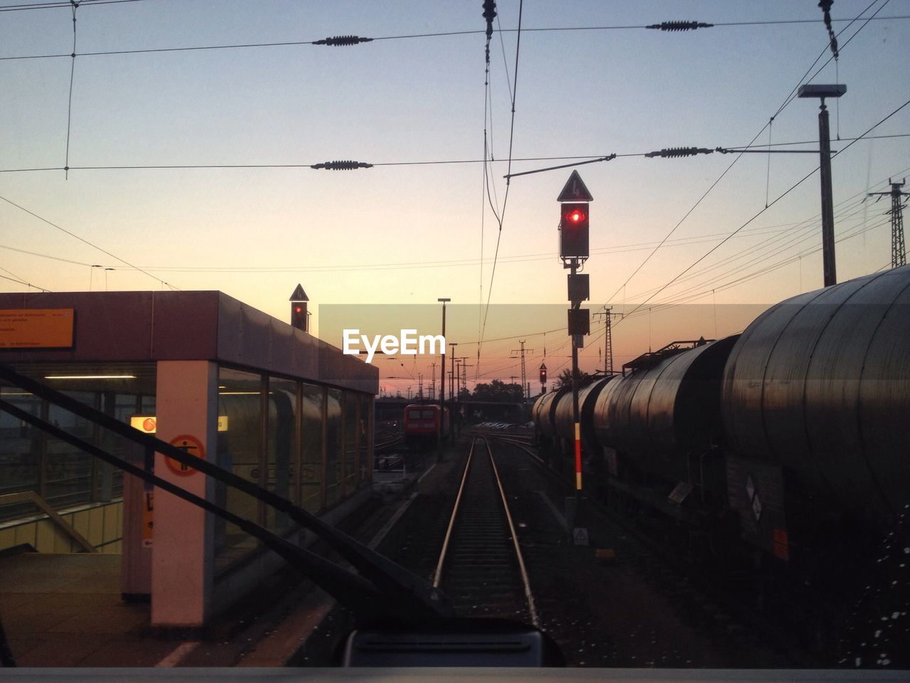 Freight train on railroad track against sky seen through windshield at sunset