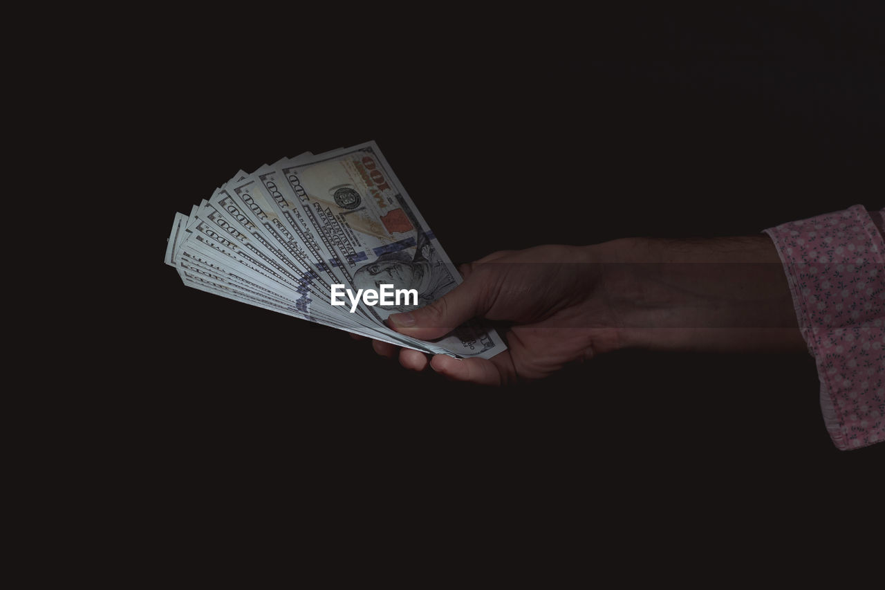 Cropped hand of woman holding us paper currency over black background