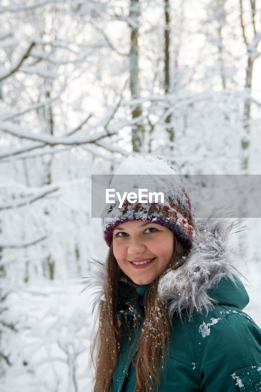portrait of smiling young woman standing against trees during winter