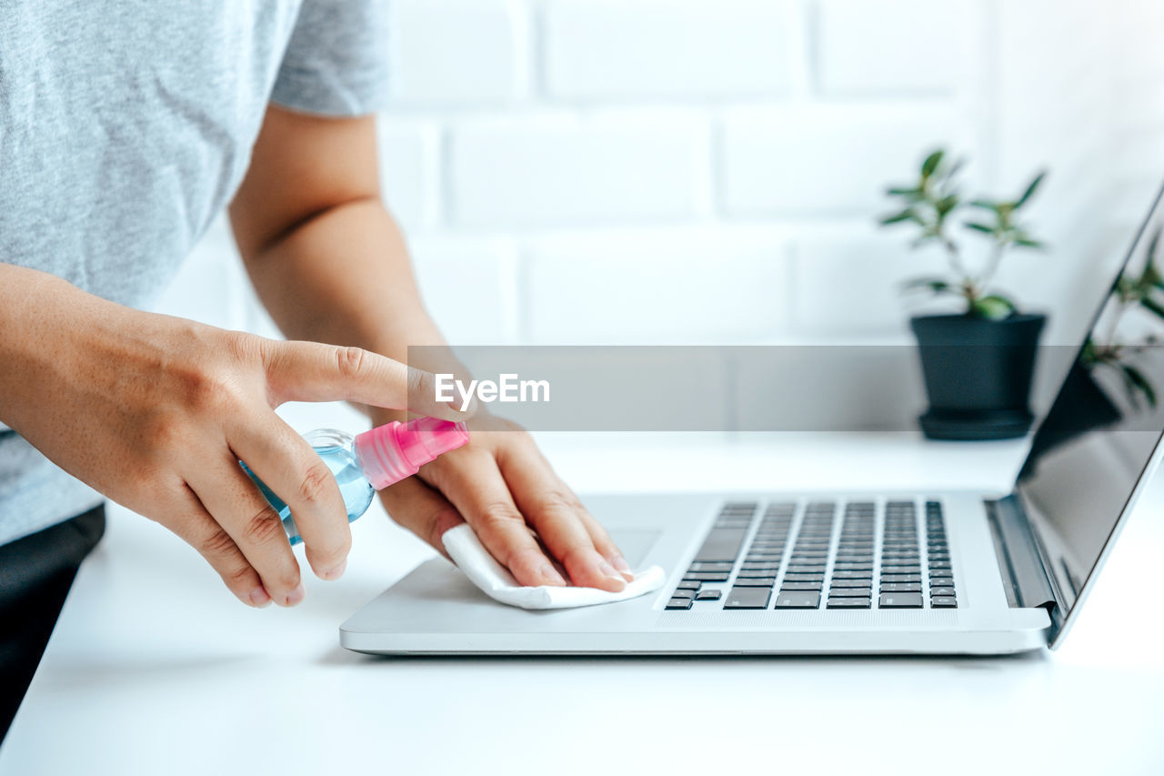 MIDSECTION OF WOMAN USING MOBILE PHONE IN LAPTOP