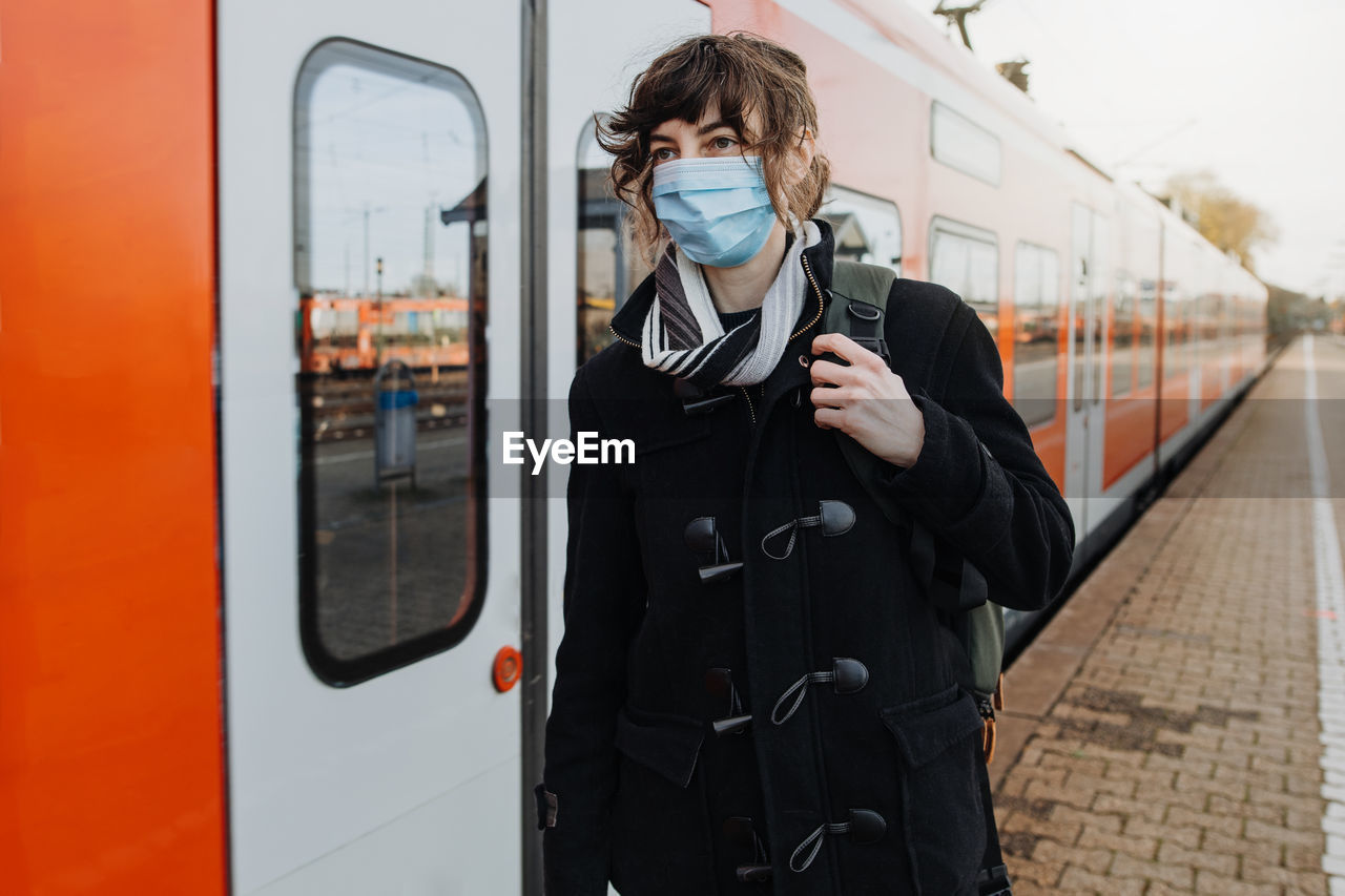 Woman wearing mask standing by train on railroad station platform