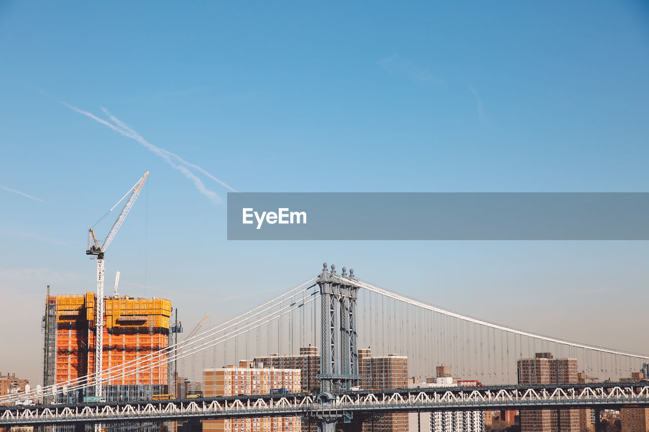 Manhattan bridge against blue sky on sunny day in city