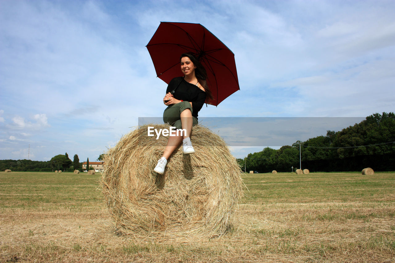 FULL LENGTH OF WOMAN ON HAY BALES FIELD