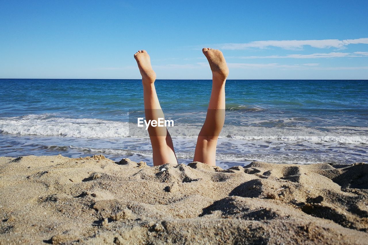 Low section of woman on beach against sky