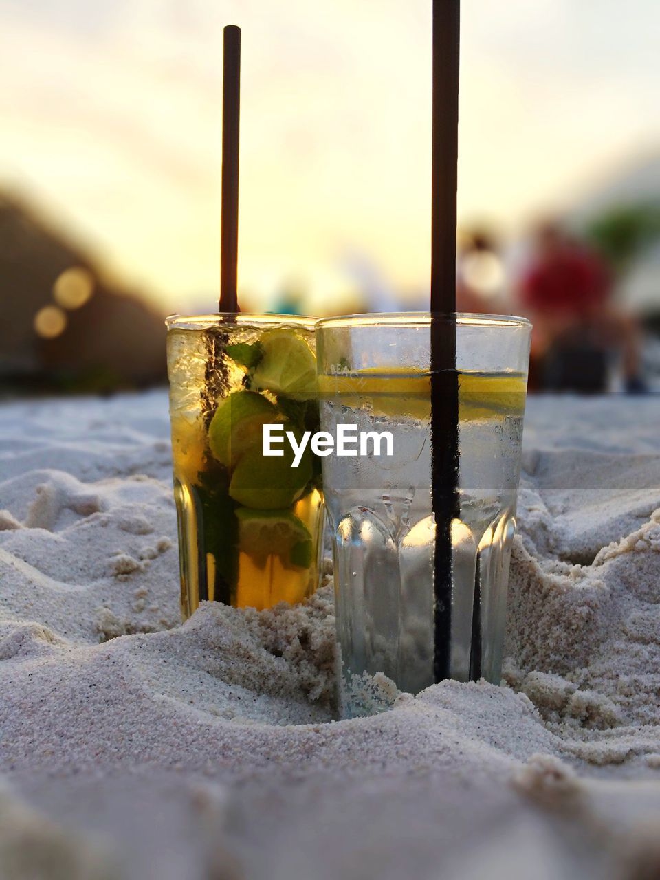 Close-up of drinks on sand at beach during sunset