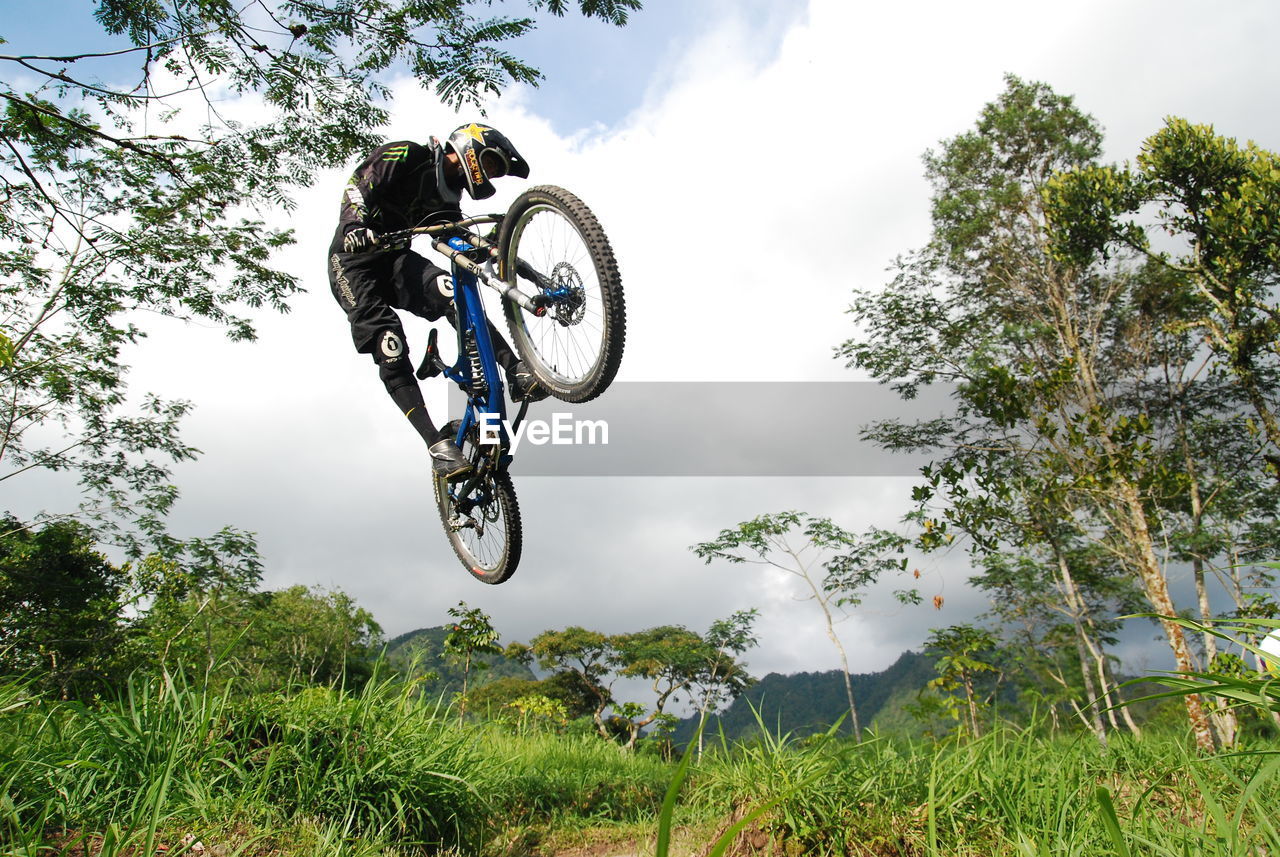 LOW ANGLE VIEW OF MAN JUMPING ON BICYCLE AGAINST SKY