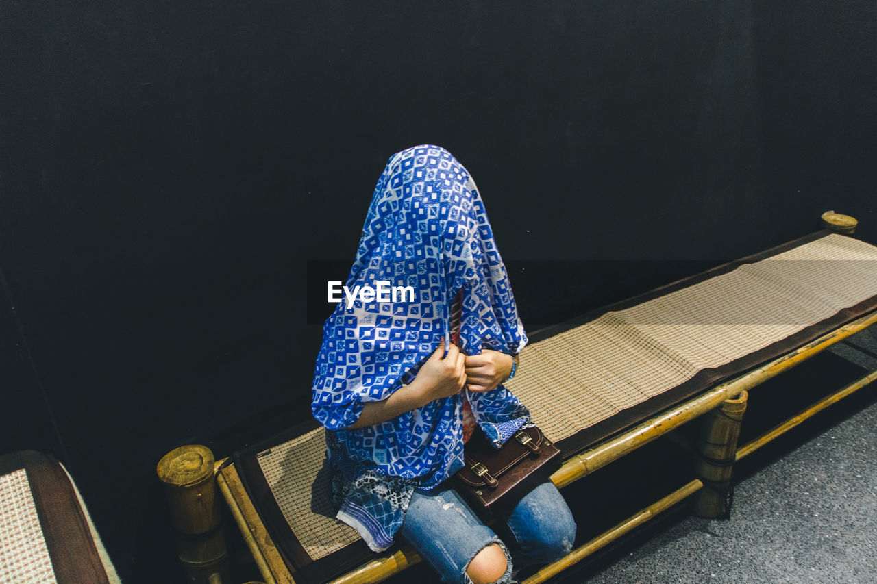 Woman covering face with scarf while sitting on bench