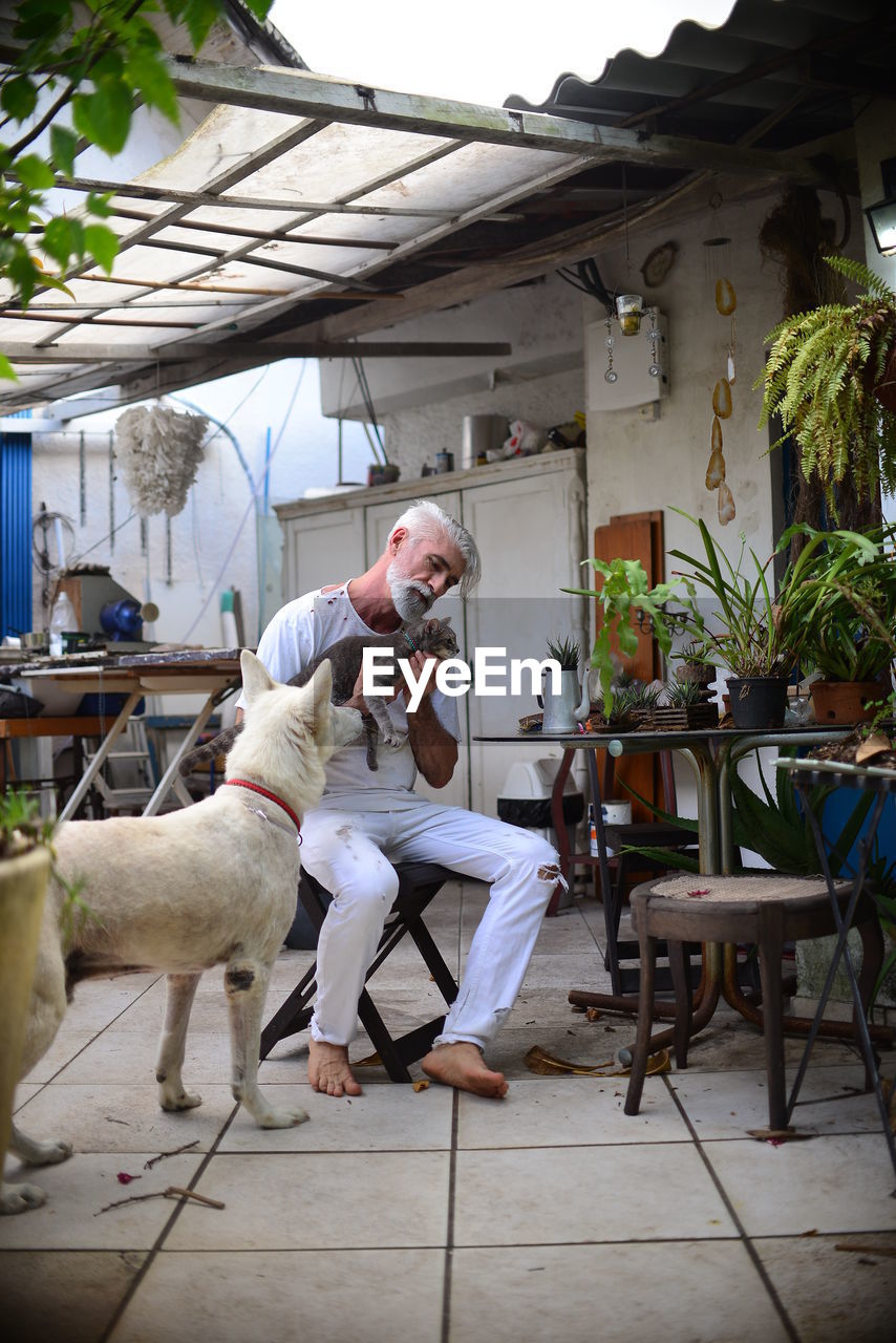 Man sitting on chair at table with cat and dog