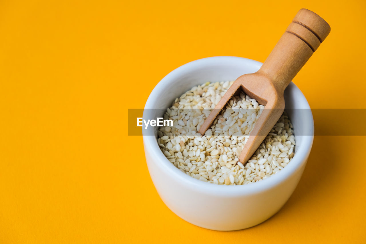 Wooden spoon with sesame seeds lies in a white mortar on a yellow background. healthy eating. keto 