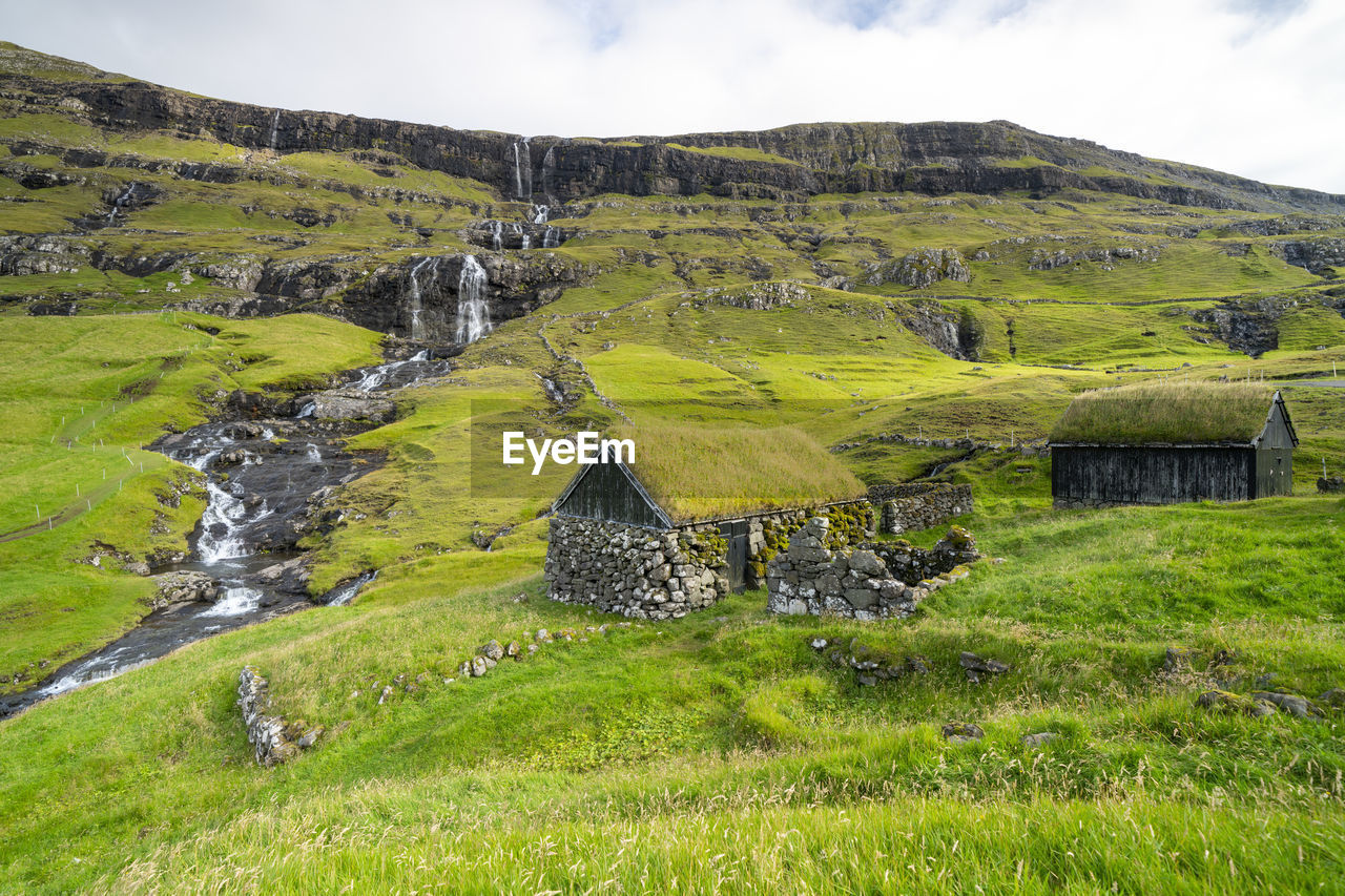 Scenic view of historical buildings with gras roof and waterfall, saksun, faroe islands.