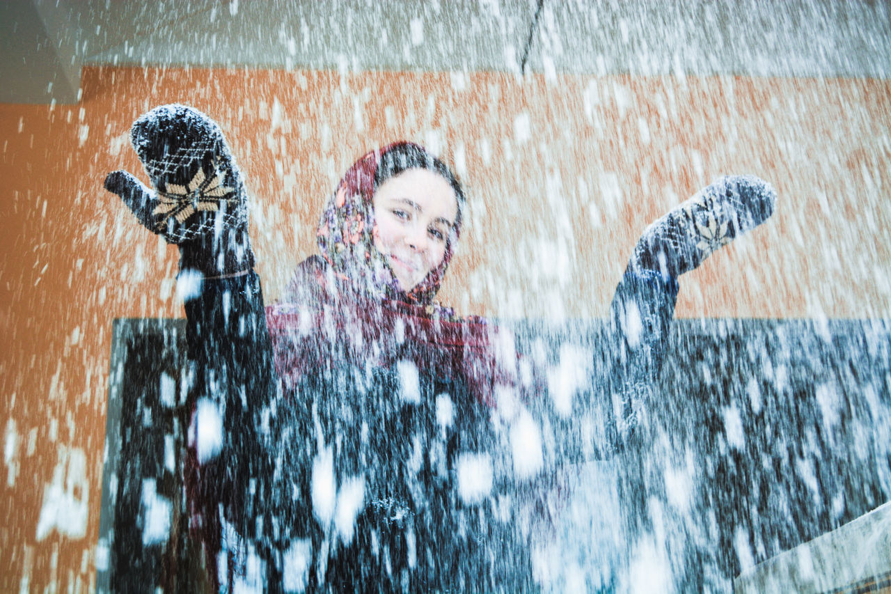 Low angle portrait of smiling woman standing outdoors during snowfall