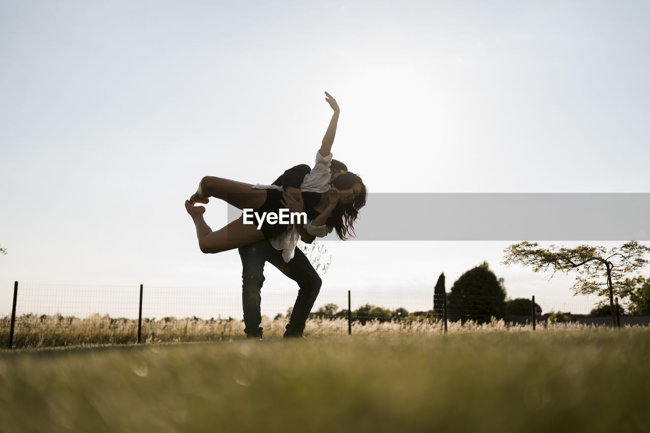 Male dancer picking up female dancer while dancing in field against clear sky