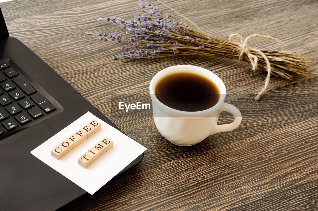 A cup of coffee near the computer and a bouquet of lavender, the inscription coffee time