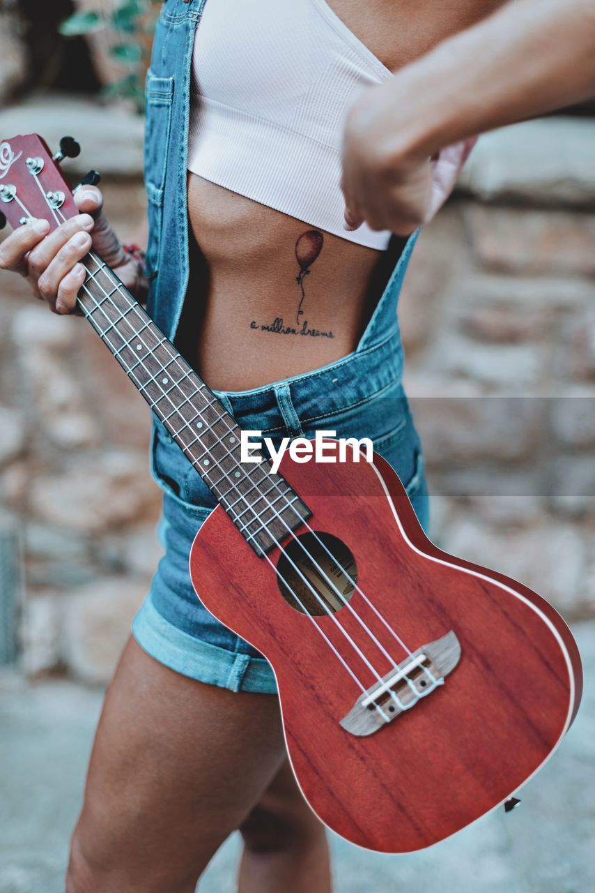 Midsection of woman showing tattoo while holding guitar
