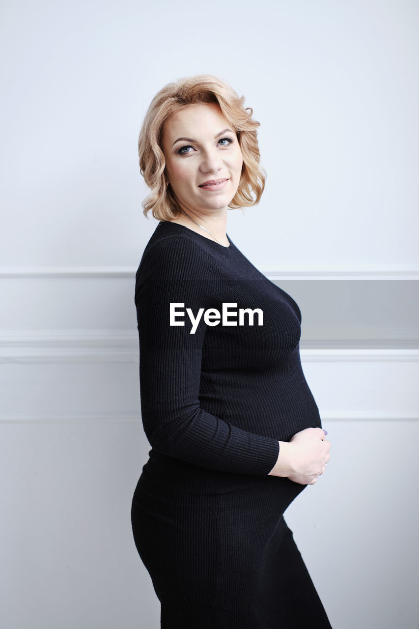 Pregnant woman in black dress smiling touching tummy