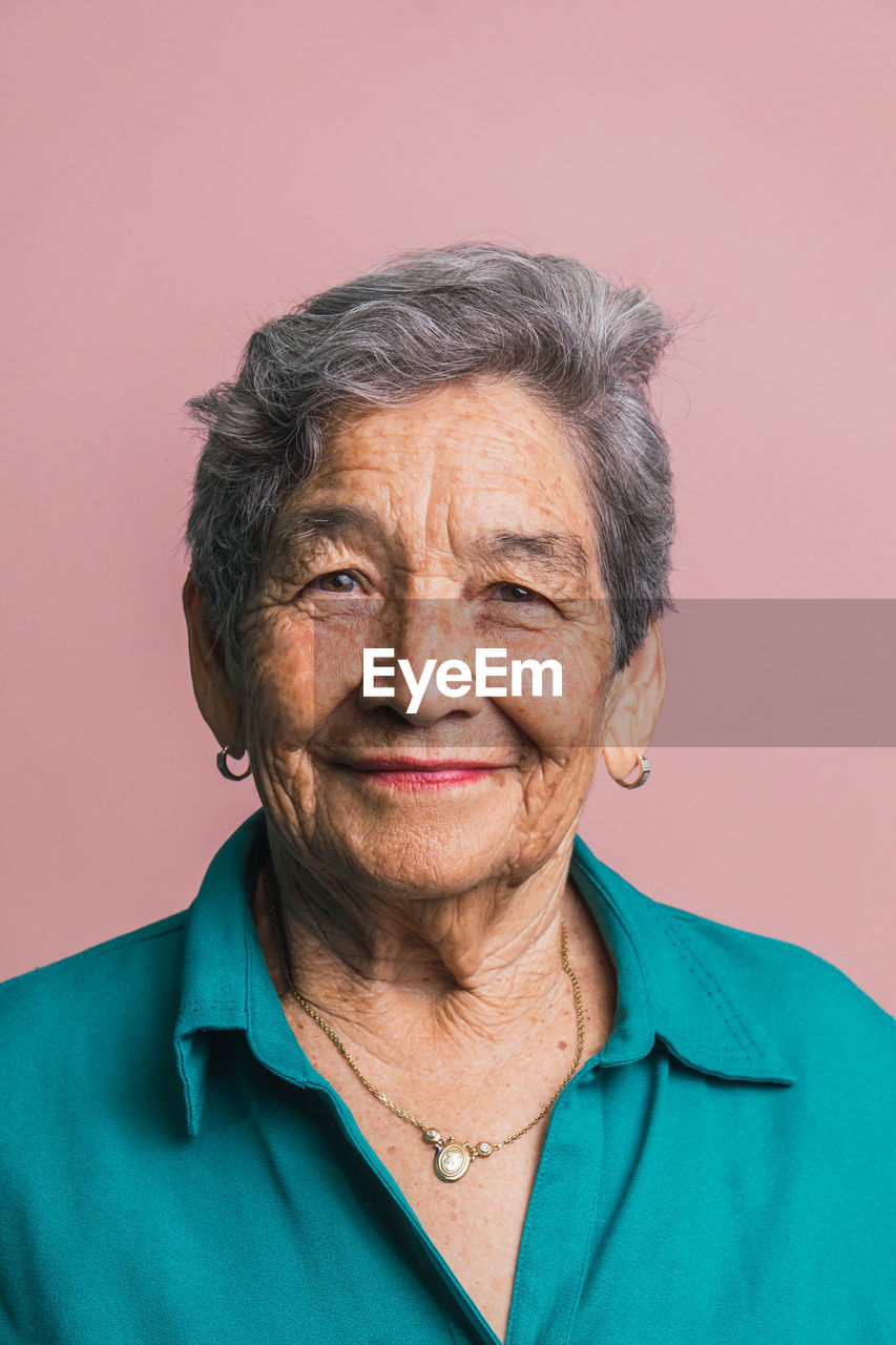 Elderly female with short gray hair and brown eyes looking at camera on pink background in studio